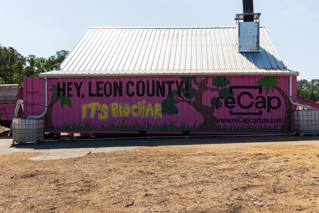 A pink building with sheet metal roofing and siding. On this side there is a mural of various trees and grass with the text "Hey Leon County, It's Biochar! www.reCapcarbon.com"